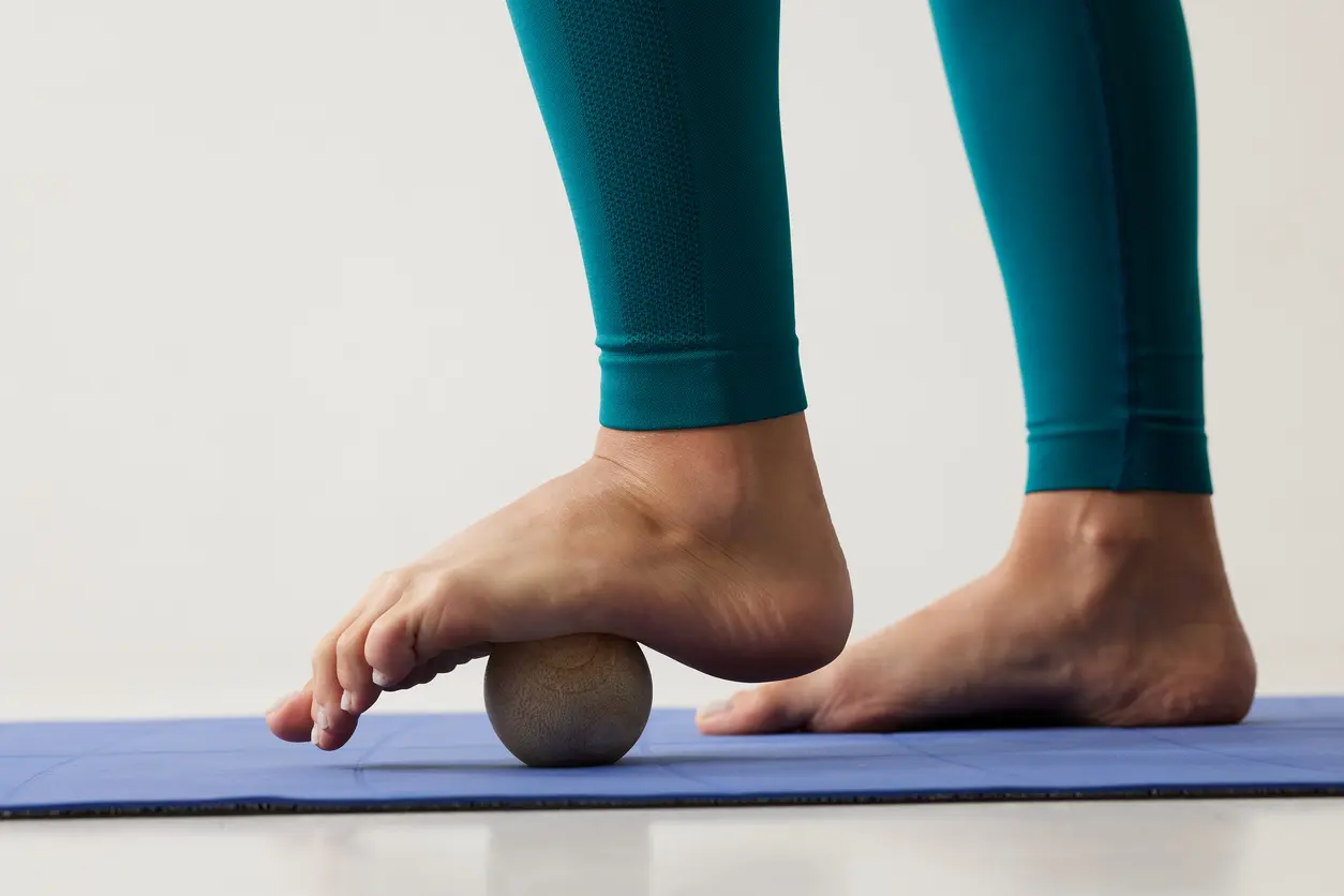 girl massaging her feet on a hard ball close-up on a white background, self-massage